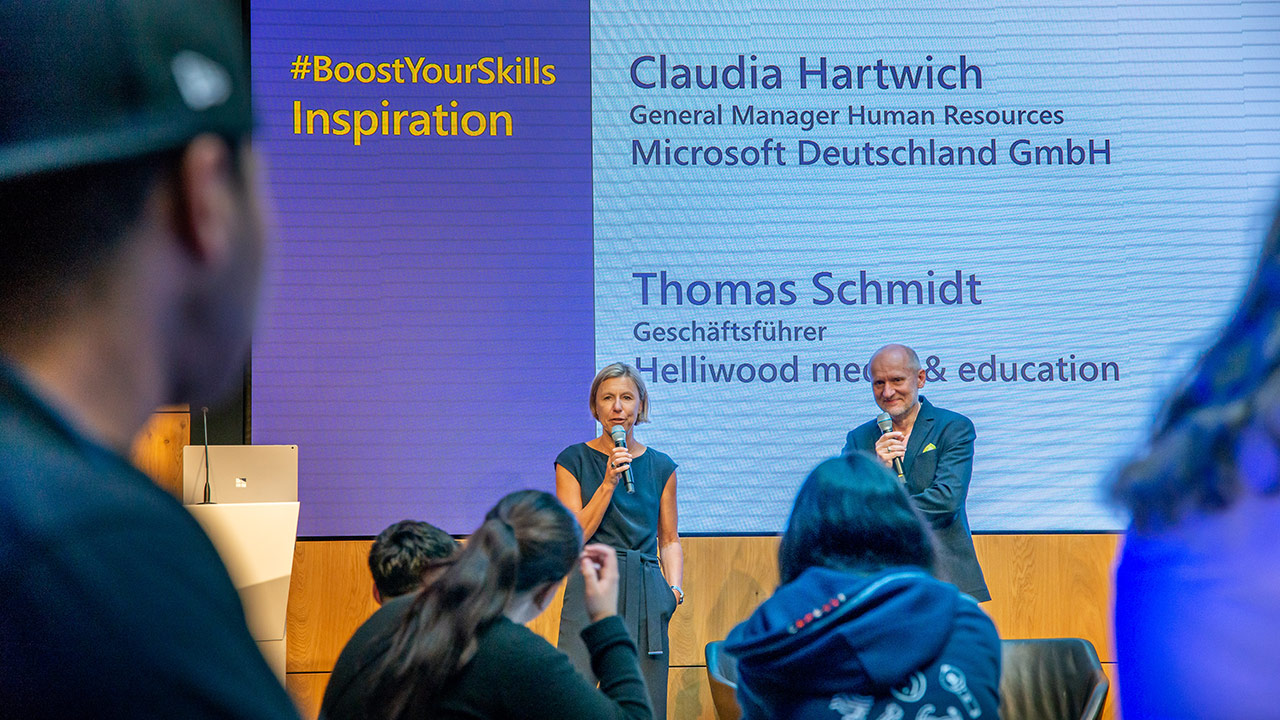 Das Foto zeigt Claudia Hartwich und Thomas Schmidt auf der Bühne des Atriums bei Microsoft Berlin