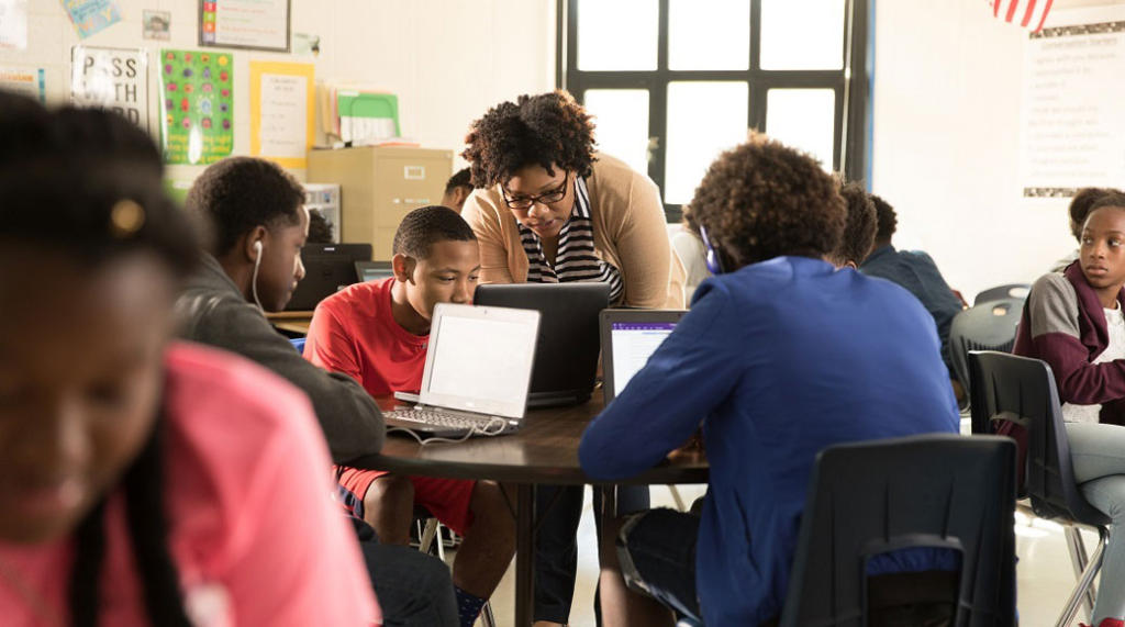 Eine Gruppe von Schülern lernen am Laptop und werden von einer Lehrerin beaufsichtigt. Eine Gruppe von Schülern lernen über Microsoft Teams und wird von einer Lehrerin beaufsichtigt.