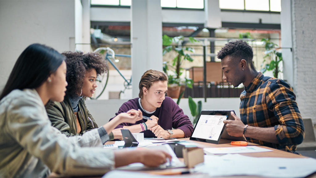 Vier Jugendliche sitzen mit einem Tablet am Tisch und diskutieren
