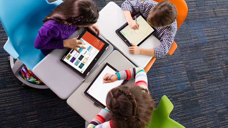 Drei Kinder sitzen an Schreibtischen und arbeiten an Tablets.