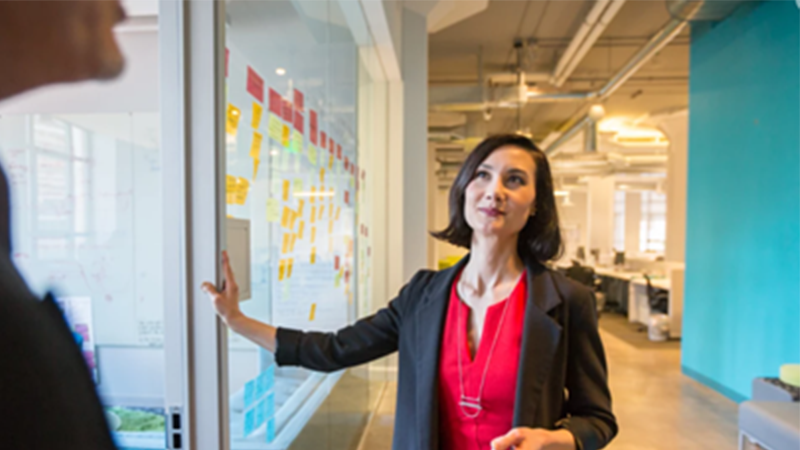 Frau steht neben einer Glaswand und spricht mit einem Mann.