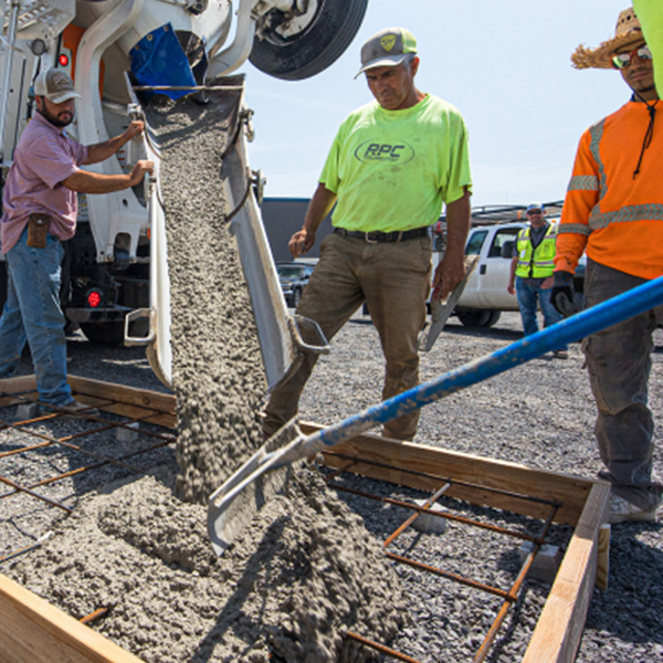 Construction workers pour concrete from a large mixing truck into a frame on the ground