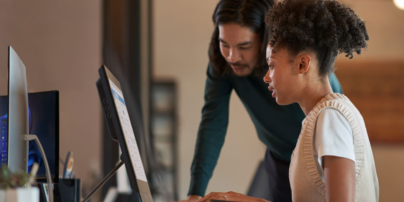 A female office worker and a male colleague look at a computer screen, discussing work