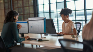 Two female office employees work at their PC screens