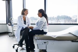 A smiling doctor talks with a woman in a hospital room.