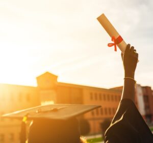 Person wearing a graduation cap and gown holds up a diploma.