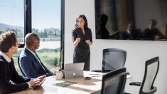 Image of a woman in a conference room presenting a topic to two seated participants