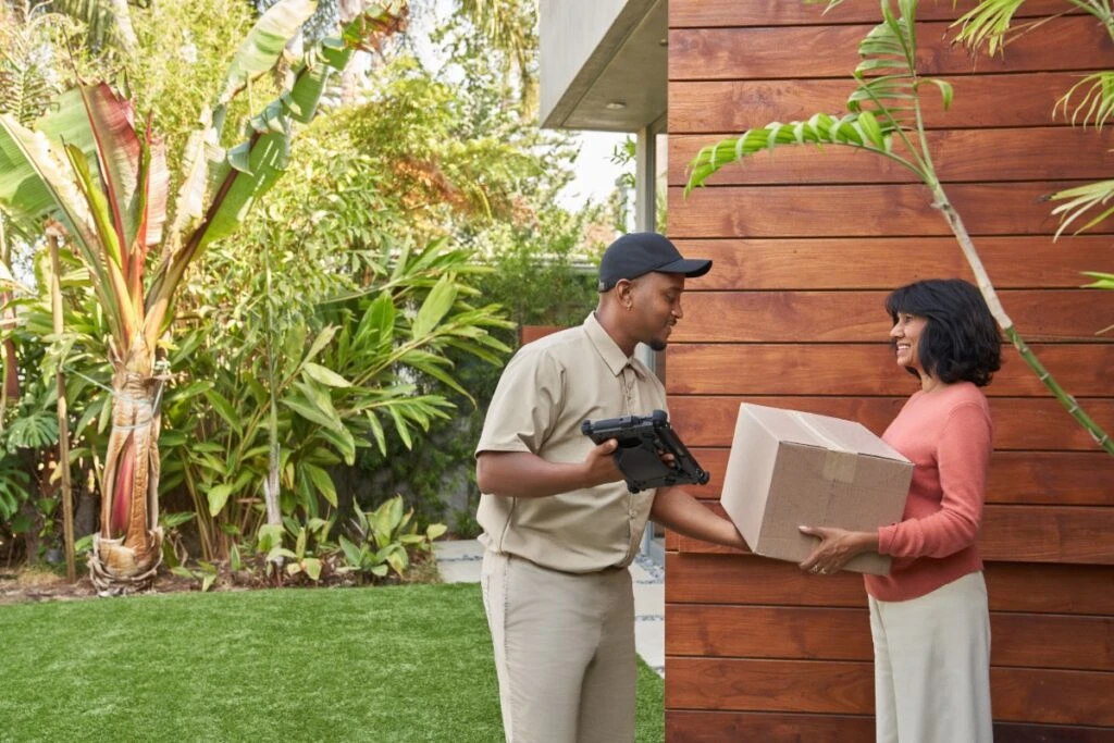 Delivery person handing a package to a satisfied customer at the customer&rsquo;s doorstep. Keywords: Dynamics 365; purchase; online ordering; ecommerce; delivering a box; Surface tablet; at home; receiving an order; driver; man; woman
