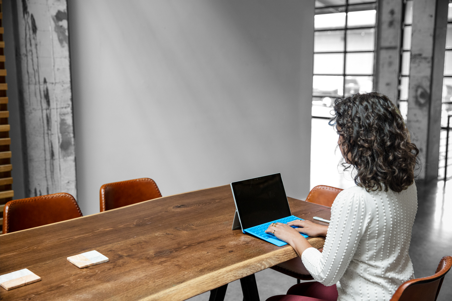 Photo looking over shoulder of female worker using computer in casual open office setting.