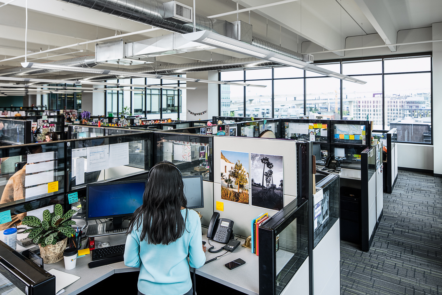 Photo of a female call center agent standing at a cubicle desk in a call center office.