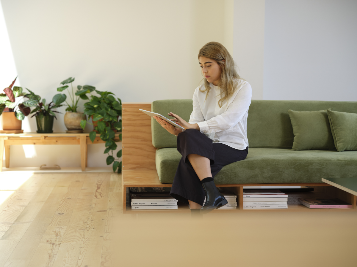 A woman sitting on a couch, working on a tablet.