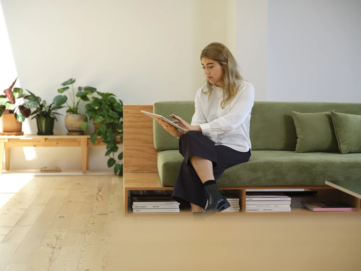 A woman sitting on a couch, working on a tablet.