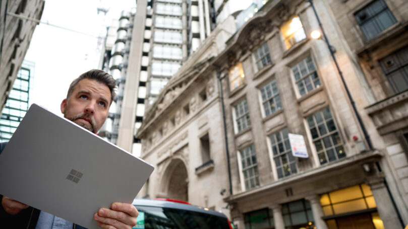 A man holding a laptop in front of a building
