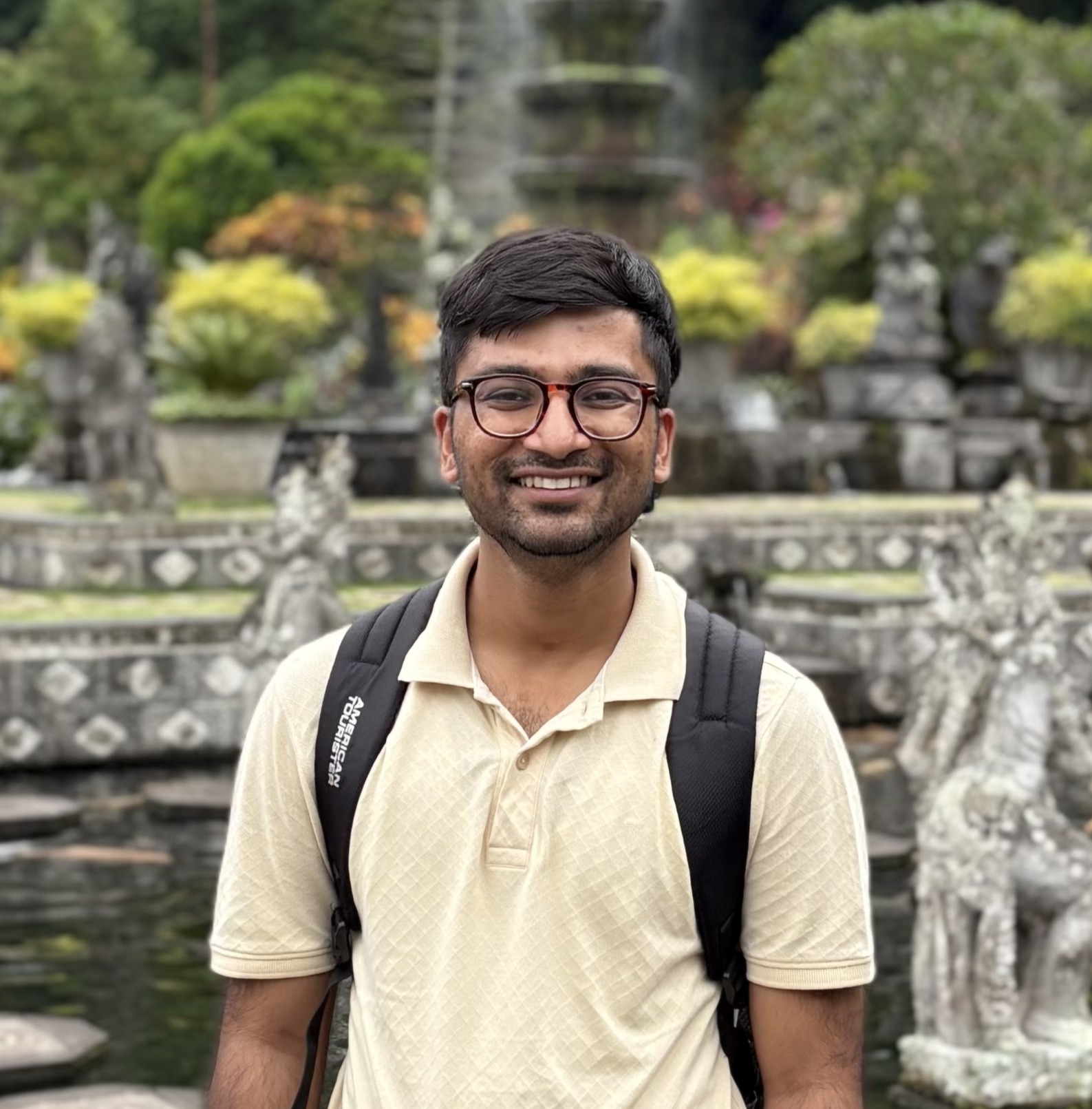 A man wearing glasses and backpack standing in front of a fountain