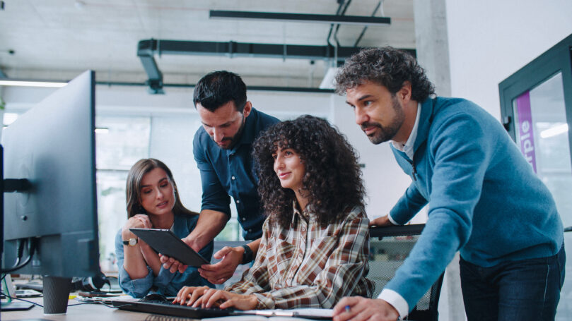 Group of smart coworkers intently looking at computer screen. People brainstorming about working plan or searching for solution to issue. Men and women positively communicating.