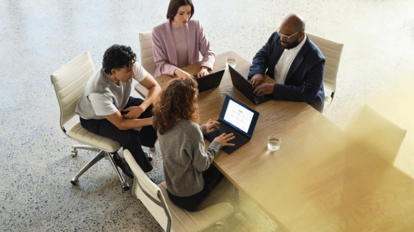 A group of people sitting at a long table, using laptops to evaluate a product and outcome