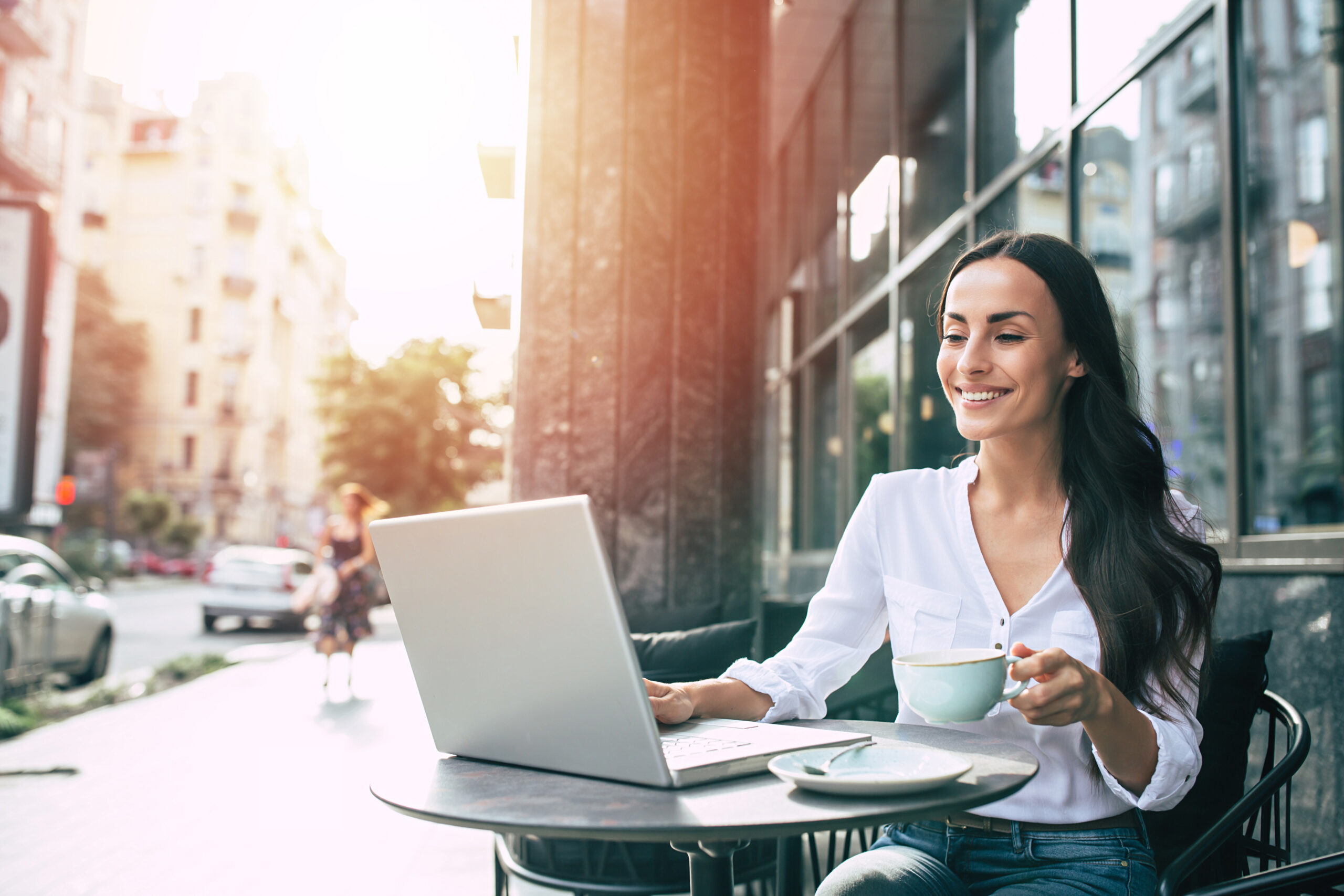 Happy beautiful young businesswoman working on laptop in street cafe outdoor