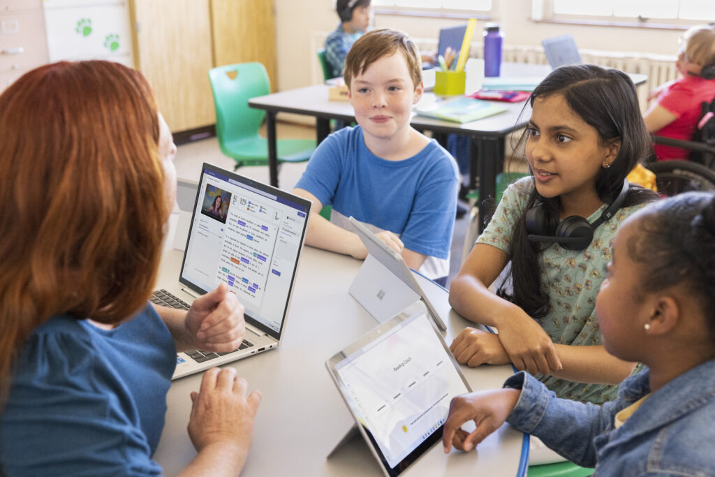 A teacher sitting at a table with a small group of students in a classroom.