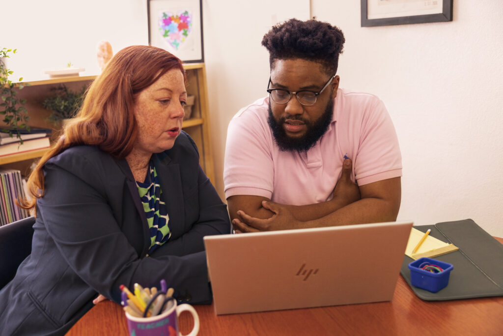 An IT team sitting in a school office and working on a laptop together.