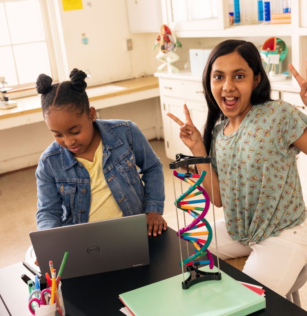 Classroom scene with two students smiling and working on a computer.