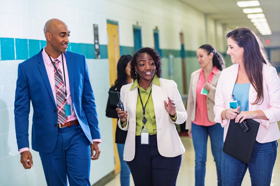 A group of education leaders and educators walking and talking together in a school hallway.