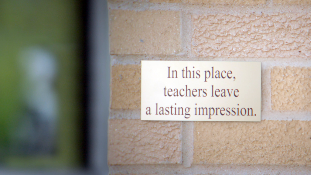 A plaque on a brick wall of a school that says, “In this place, teachers leave a lasting impression.”