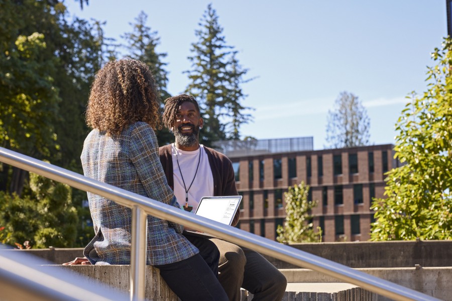 Two higher education leaders with a laptop sit outside together in a university setting.