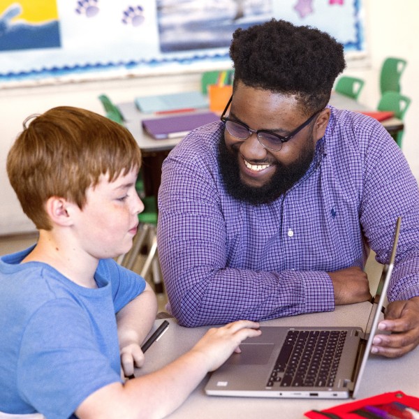 An educator engaging with a student at the student’s desk in a school classroom.