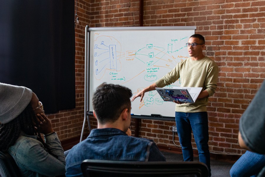 A worker holds a laptop while presenting to a team during a meeting.