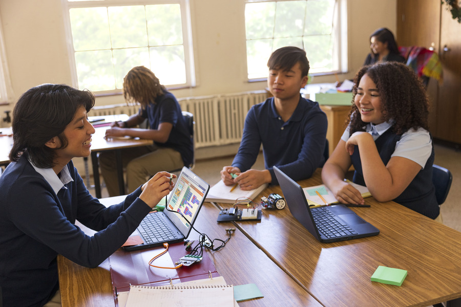 Three students sitting at a table with laptops showing Microsoft MakeCode.