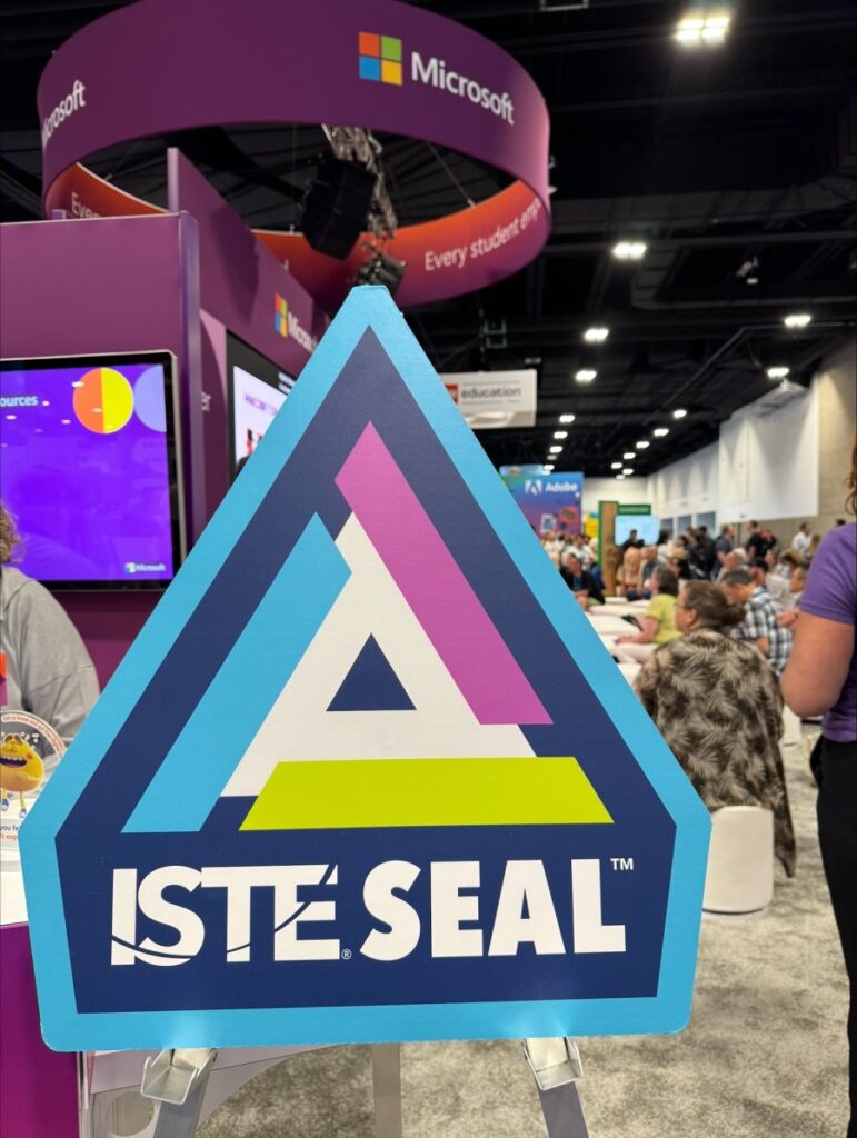 Decorative. A colorful sign with the words ISTE Seal on it, with a conference floor full of attendees in the background.