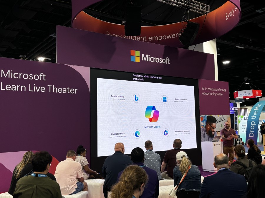 Decorative. Conference attendees sitting in a theater facing a big screen while a presenter engages with the crowd.