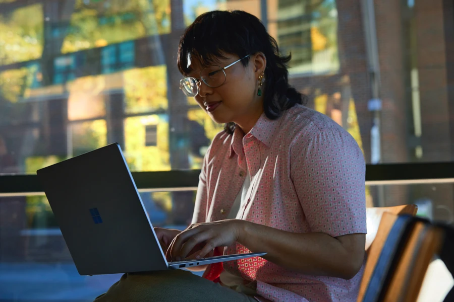 Decorative. A student typing on a laptop while seated inside a common area at a university.