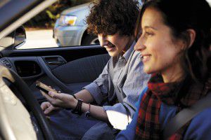 Picture of two people inside a vehicle. One is driving and one is holding a cell phone.