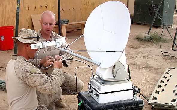 A couple of military officers working with an antenna on the ground