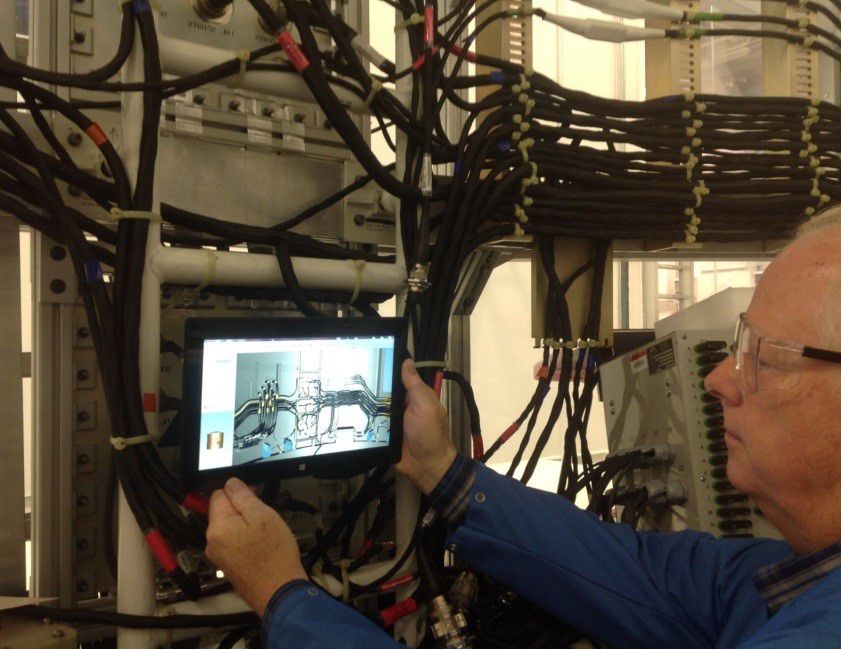 A man holding a tablet and inspecting some cable wires