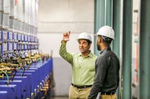 Two men wearing hard hats, talking on a work site.