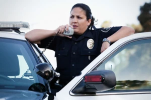 female police office standing behind police car door talking on a radio.