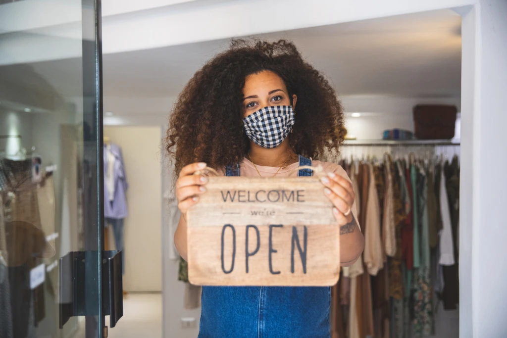 Woman holding Open sign in a small business boutique shop after Covid-19 pandemic