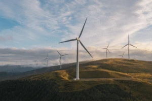Wind turbines on rolling hills at sunrise, generating renewable energy above a forested landscape.