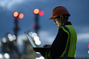Boosting Key Front-line Operations Through Digitization to Driving Sustainability in Oil and Gas Industry. Side view of Engineer working over a laptop computer to analyze insights related to the production of energy in field operation.