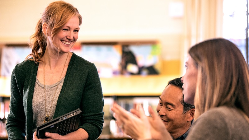 Eine Lehrerin mit Tablet erklärt einer Schülerin etwas. Lehrerinnen und Lehrer arbeiten zusammen: Kostenfreie Schulung im Umgang mit Microsoft Teams von Capgemini.