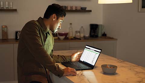 A man sitting in a kitchen who is looking at a Laptop