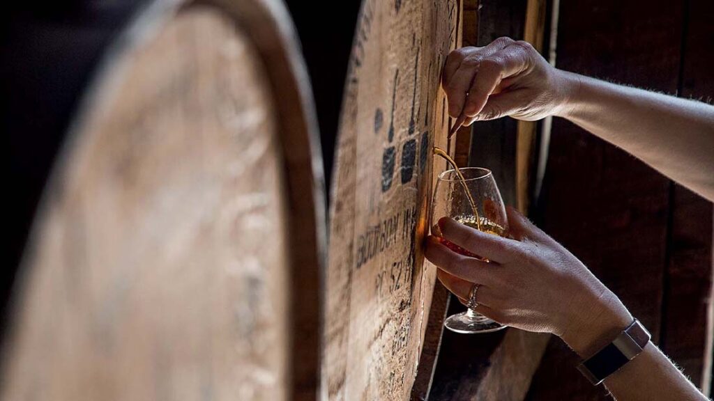 Jemand entnimmt eine Probe aus einem Whiskey Fass. 