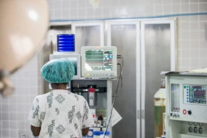Back of female nurse shown using medical equipment in medical facility.