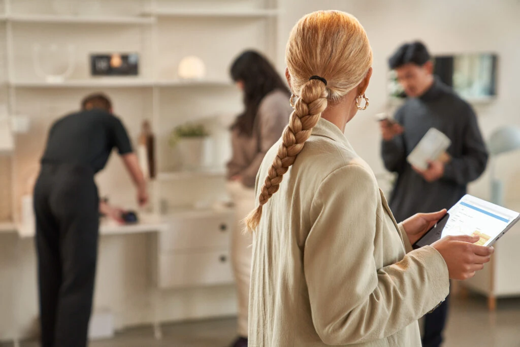 Retail worker looking at a tablet while people shop in the background.