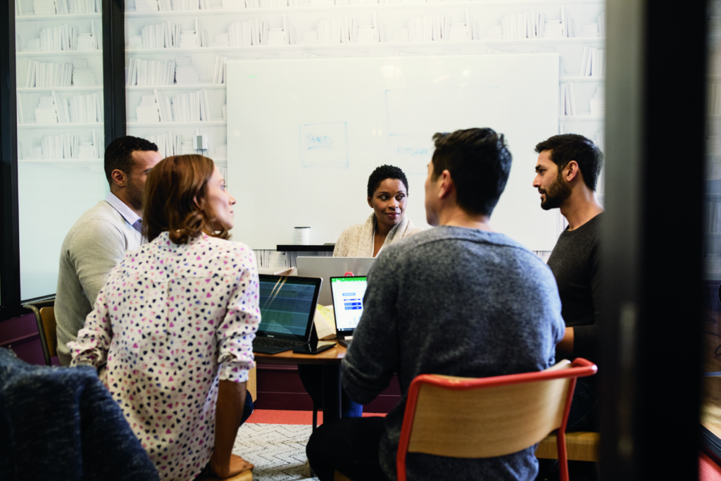 Group of five people in a meeting around a desk.