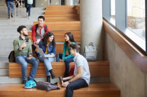 A group of male and female students seated together in an indoor common area on a university campus.