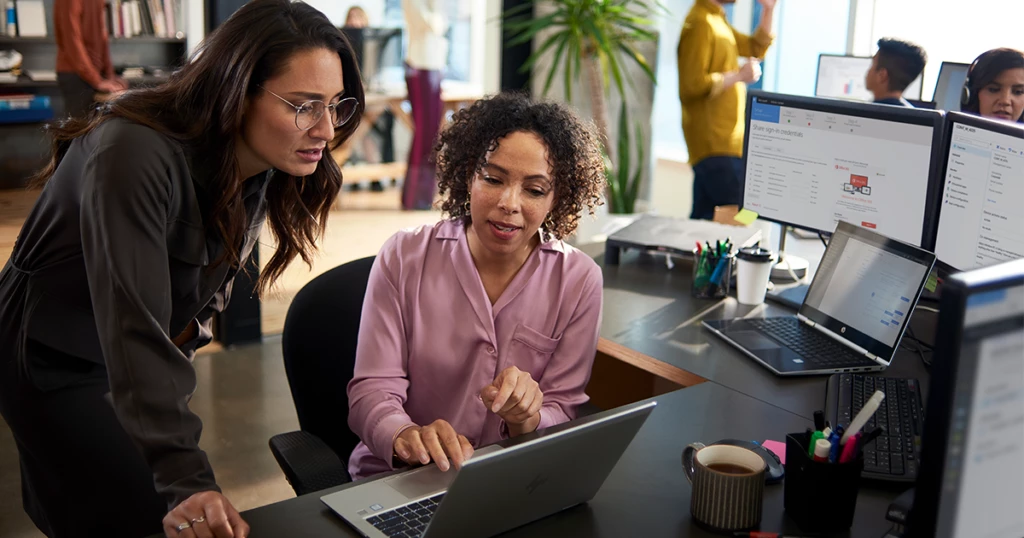 Professionals collaborating at a laptop in an open office setting.