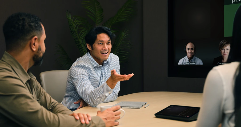 A man sitting at a table with a laptop and a man talking